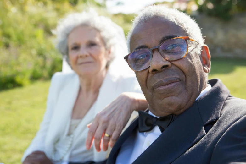 an elderly man and woman sit in a park