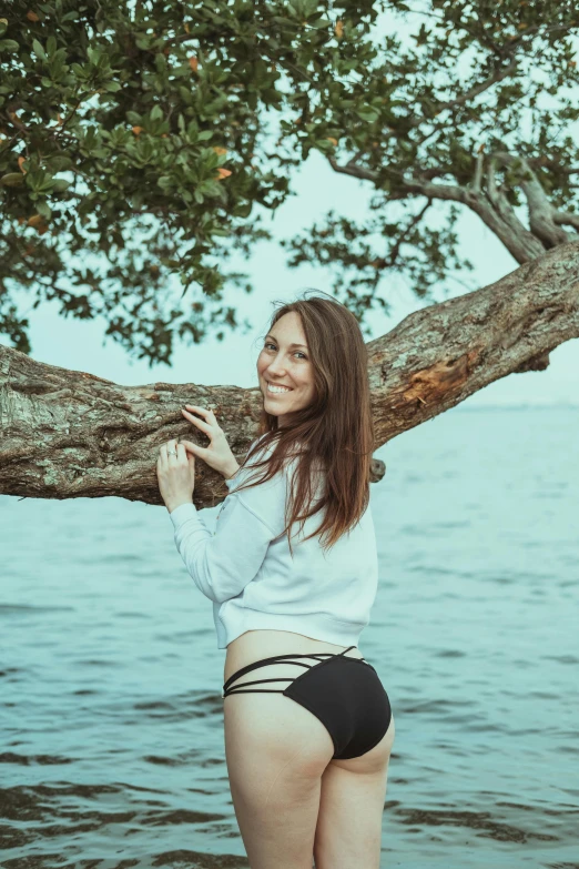 a woman posing next to the water near a tree