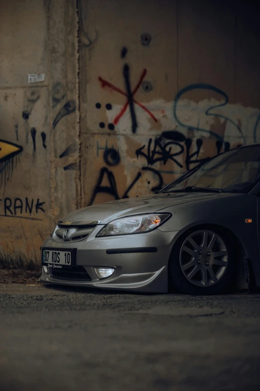 a small silver car parked in front of a graffiti covered wall