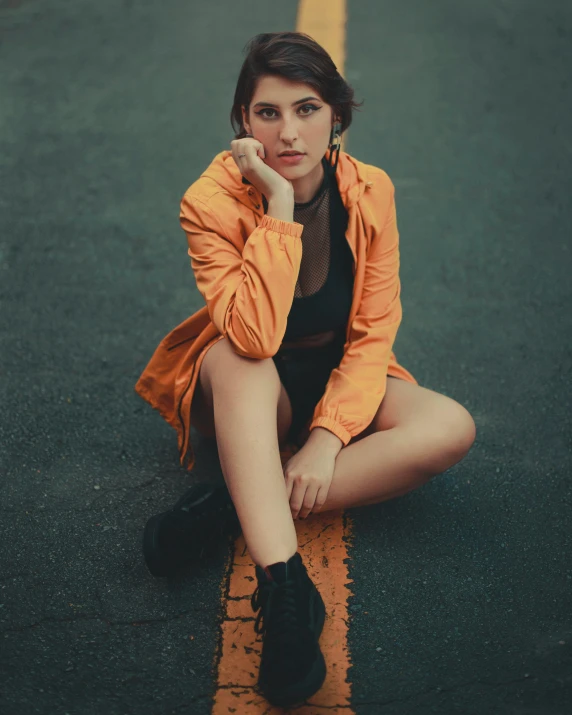a young woman wearing an orange jacket sitting on the road