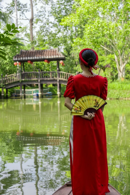 a woman in a red dress holding an oriental fan is looking at a pond