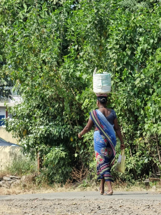 a woman carrying a basket on her head walks down the road