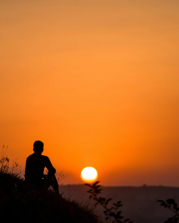 a man sitting at the top of a hill watching the sun set