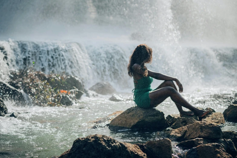 a  is sitting on rocks by a waterfall