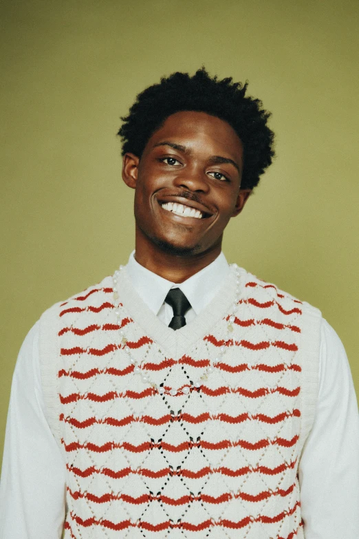 a man with curly hair smiles in a knit vest