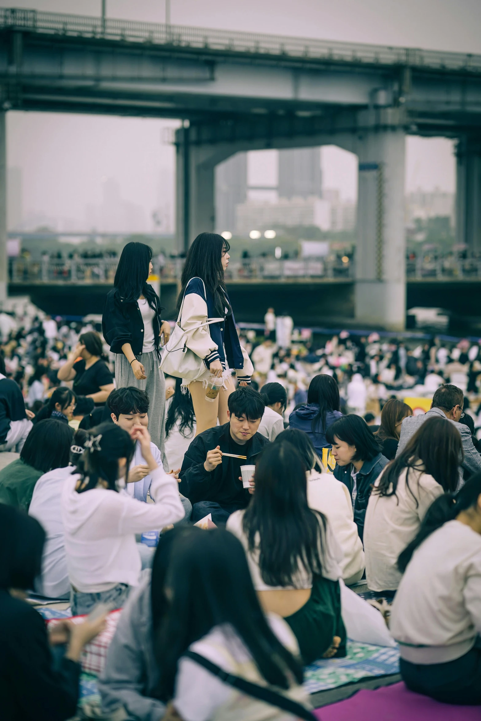 people sitting on the ground near an overpass with a sky lift overhead