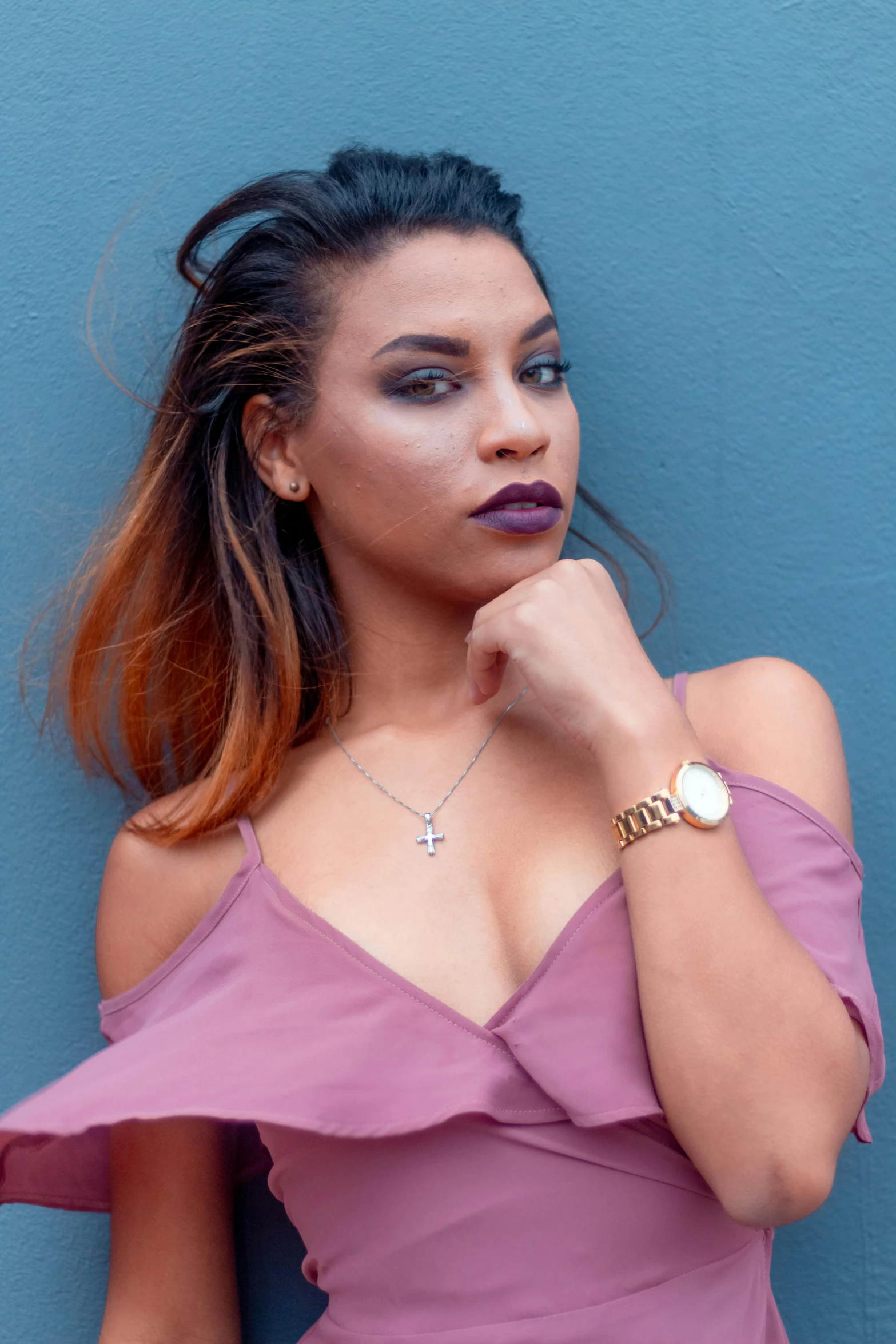 a woman wearing a pink dress and a blue background poses in front of a wall