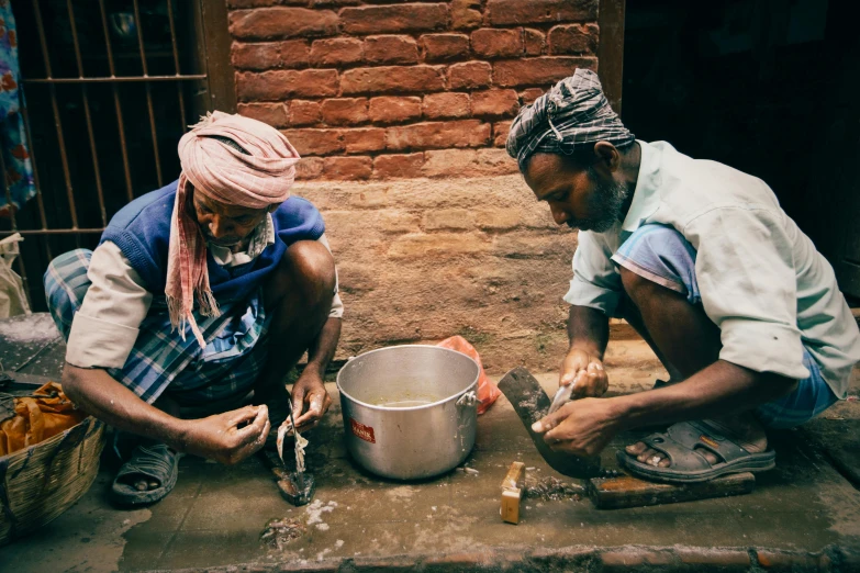 two people sit on the floor next to a metal pot