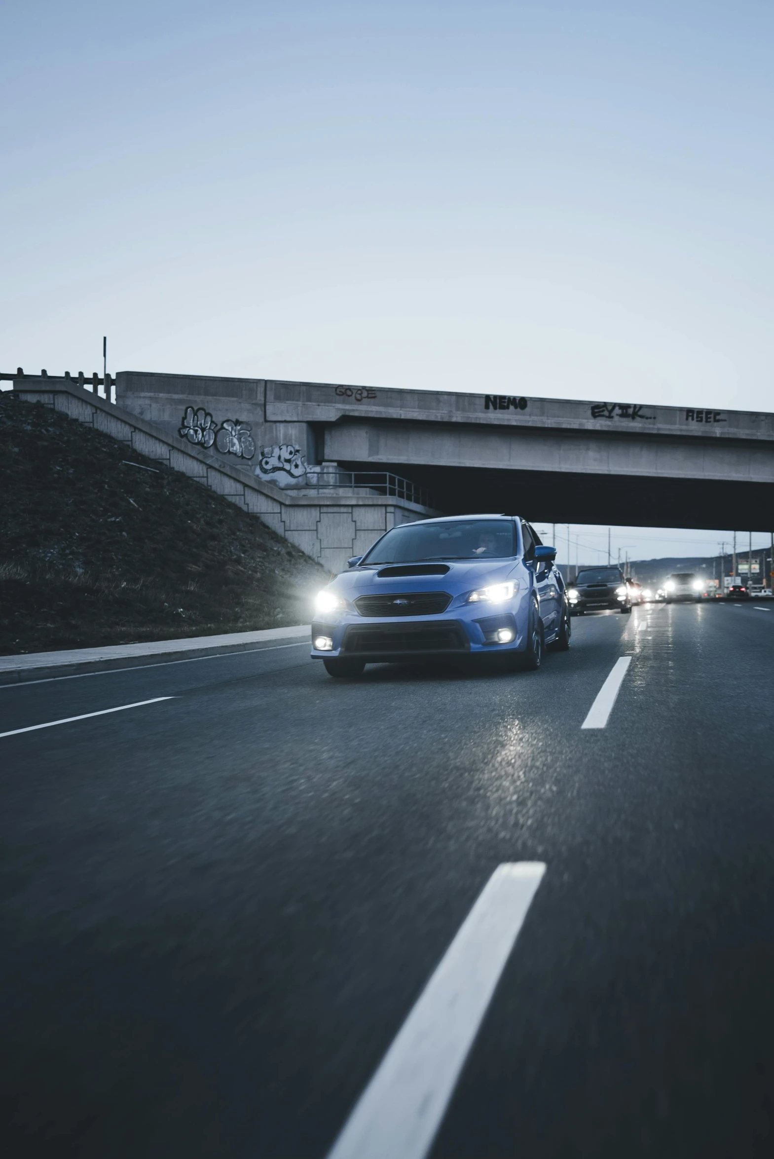 a blue vehicle driving under a bridge next to a street