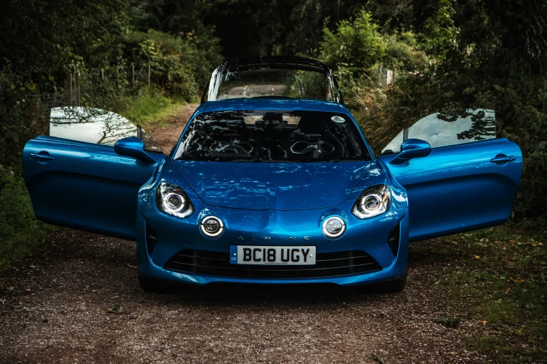 a blue car with its doors open, on the side of a dirt road