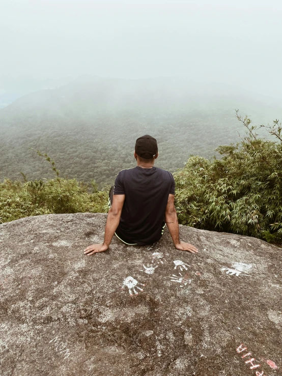 man sitting on rock with fog in the valley