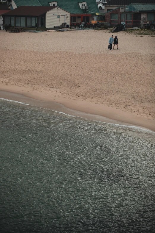 two people walking on a beach near the water