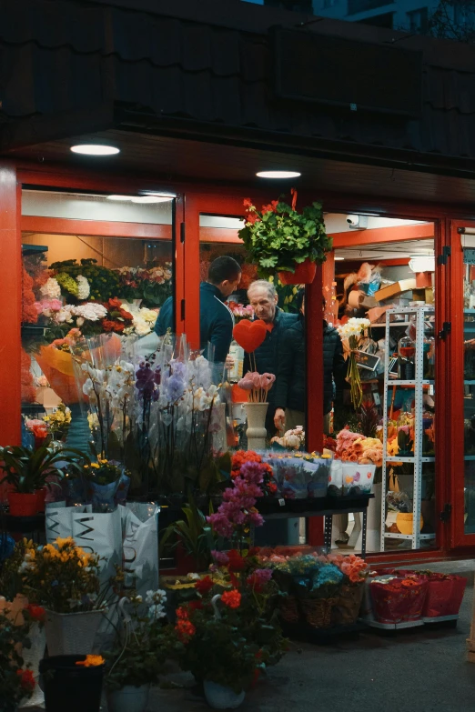 a flower shop that is red with people standing inside it