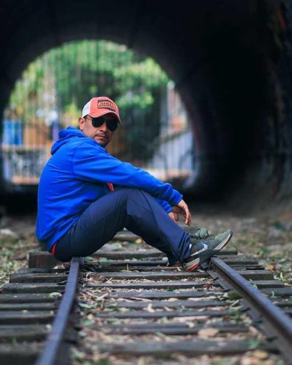 a man sits on train tracks as he watches a train roll by