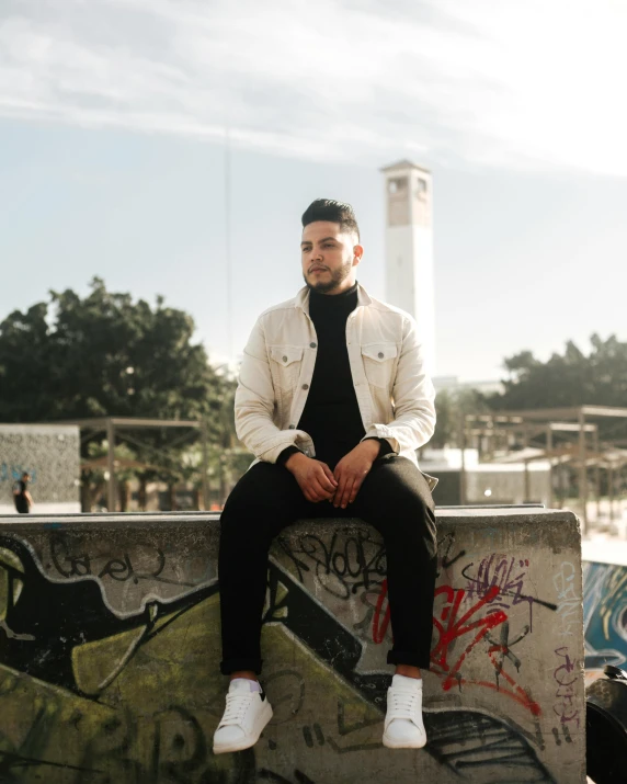 a young man is sitting on a concrete ledge in a black shirt and white shoes