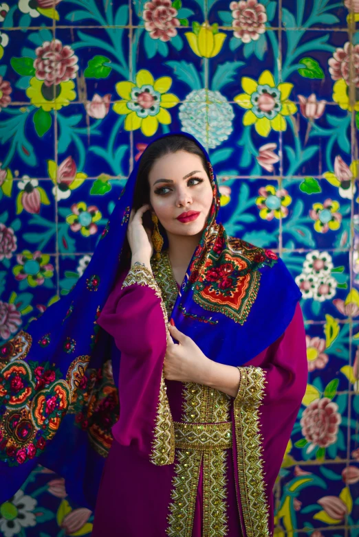the young woman in a colorful outfit stands near a blue wall with flowers