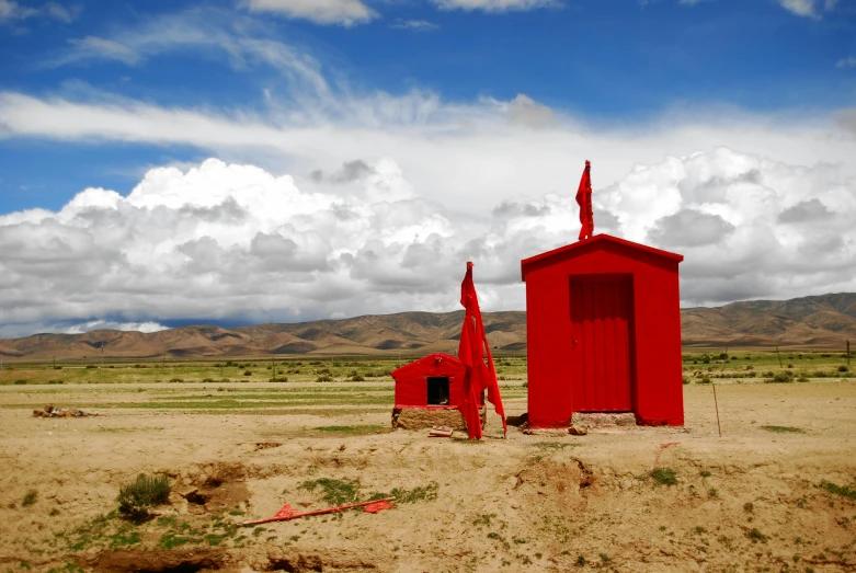 red structure in field with mountains and cloudy sky