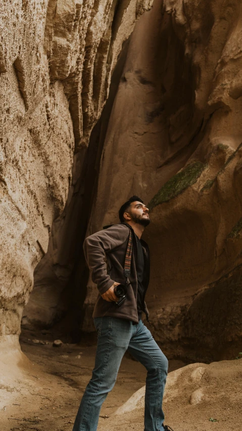 a man in a brown jacket and blue jeans poses in the desert