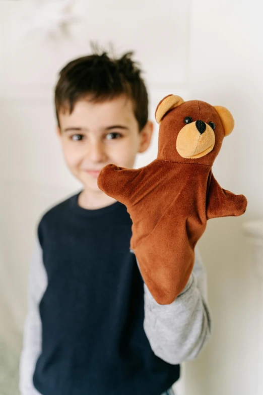 the child is holding up a brown teddy bear