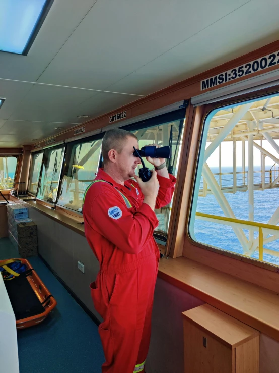 a person in red overalls holding a camera next to a window