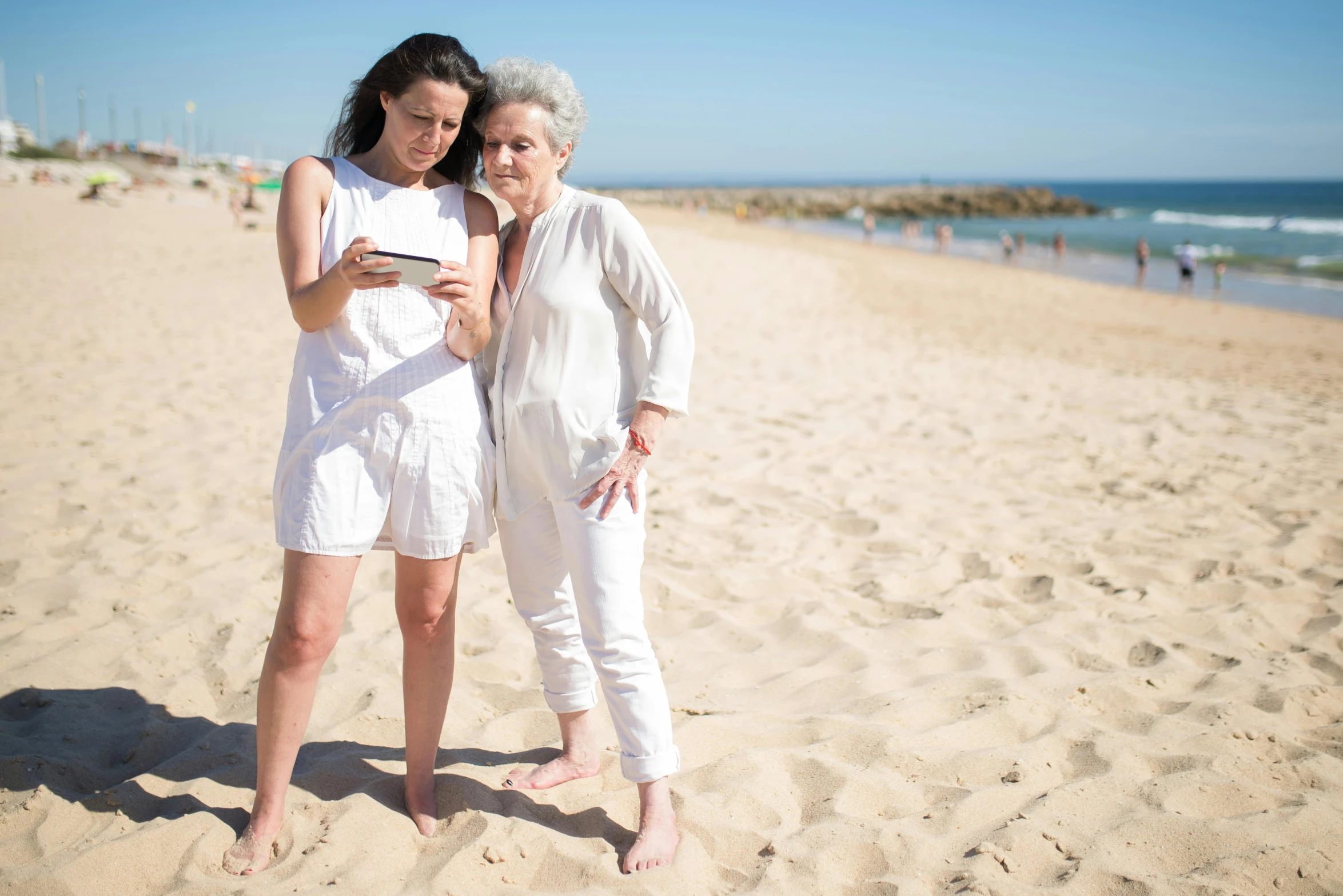 two women stand on the beach and take pictures