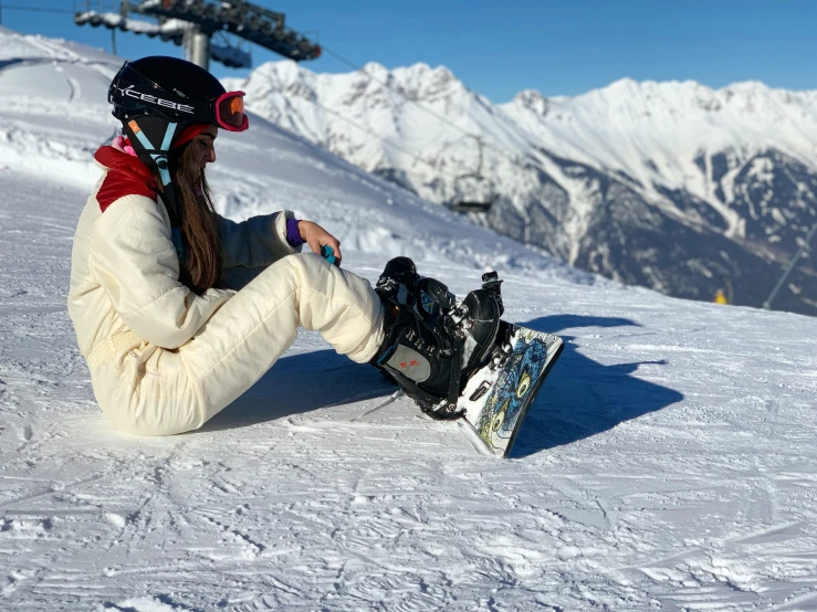 the woman sits on the snow, with her snow board in hand