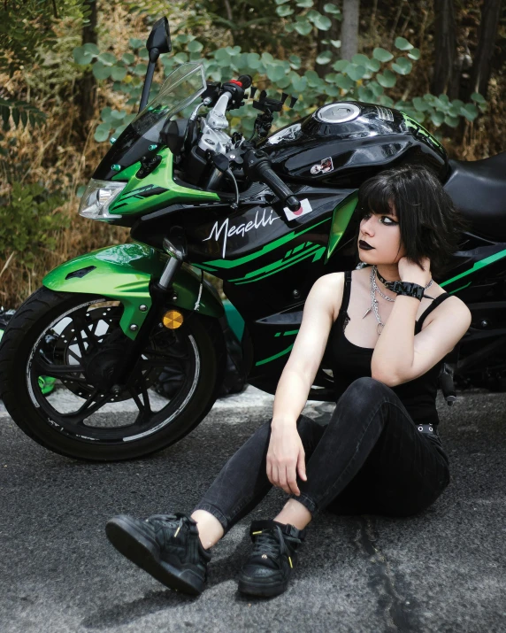 a woman sits on the ground with her legs crossed next to a motorcycle
