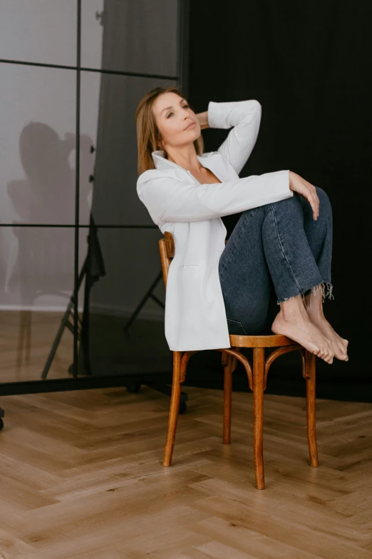the woman is wearing jeans and jacket sitting on a chair