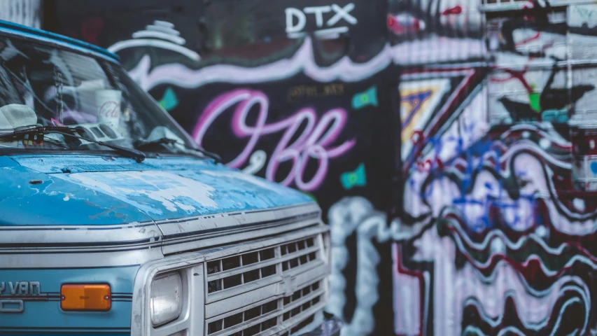 a blue van is parked in front of a wall full of graffiti