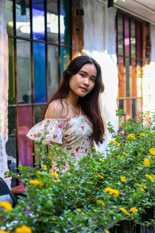 a young woman standing behind a bush in front of a window