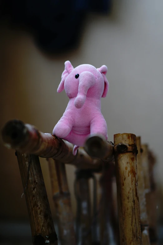 a small pink elephant sitting on a wooden fence