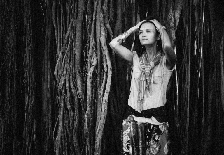 a woman standing in a forest of trees holding her head