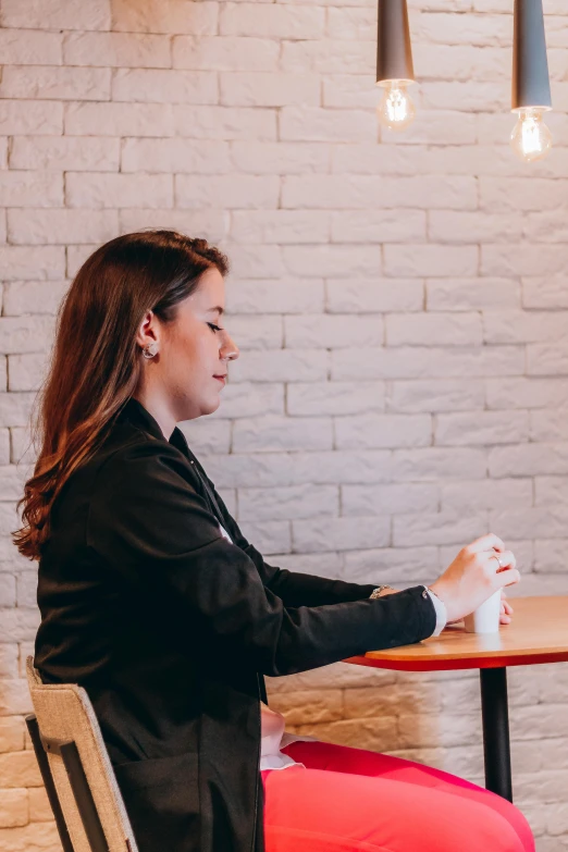 a woman sitting at a table with red pants and a black jacket