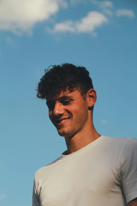 a man smiling with blue sky and white clouds in the background