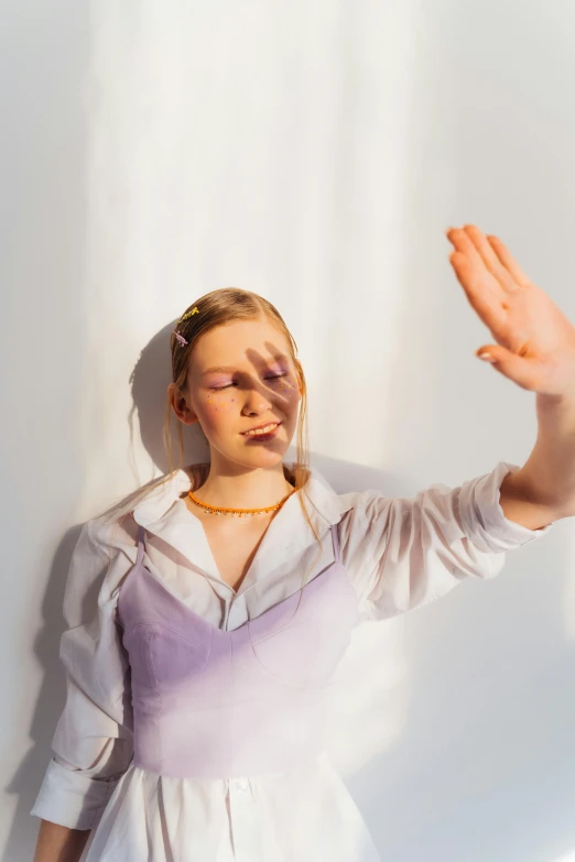 woman in white dress with hands up against a wall