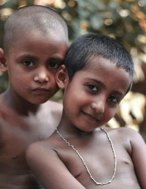 two boys are pictured in close proximity, one has a chain around his neck