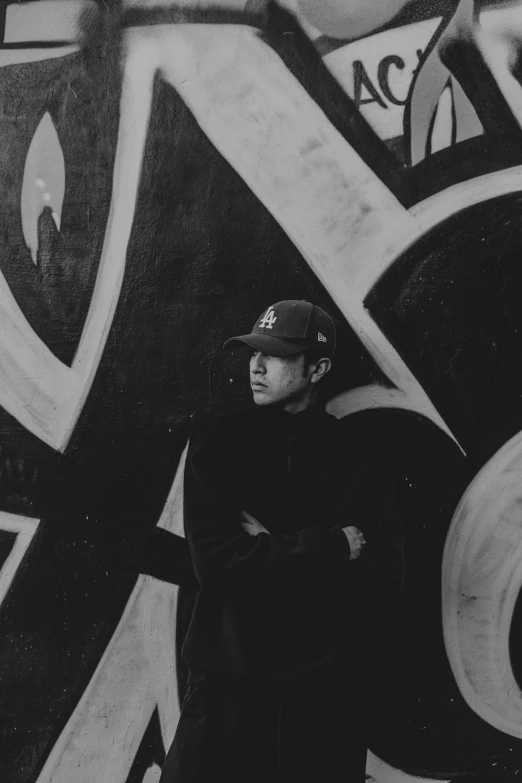 a young man wearing a cap standing next to some graffitti