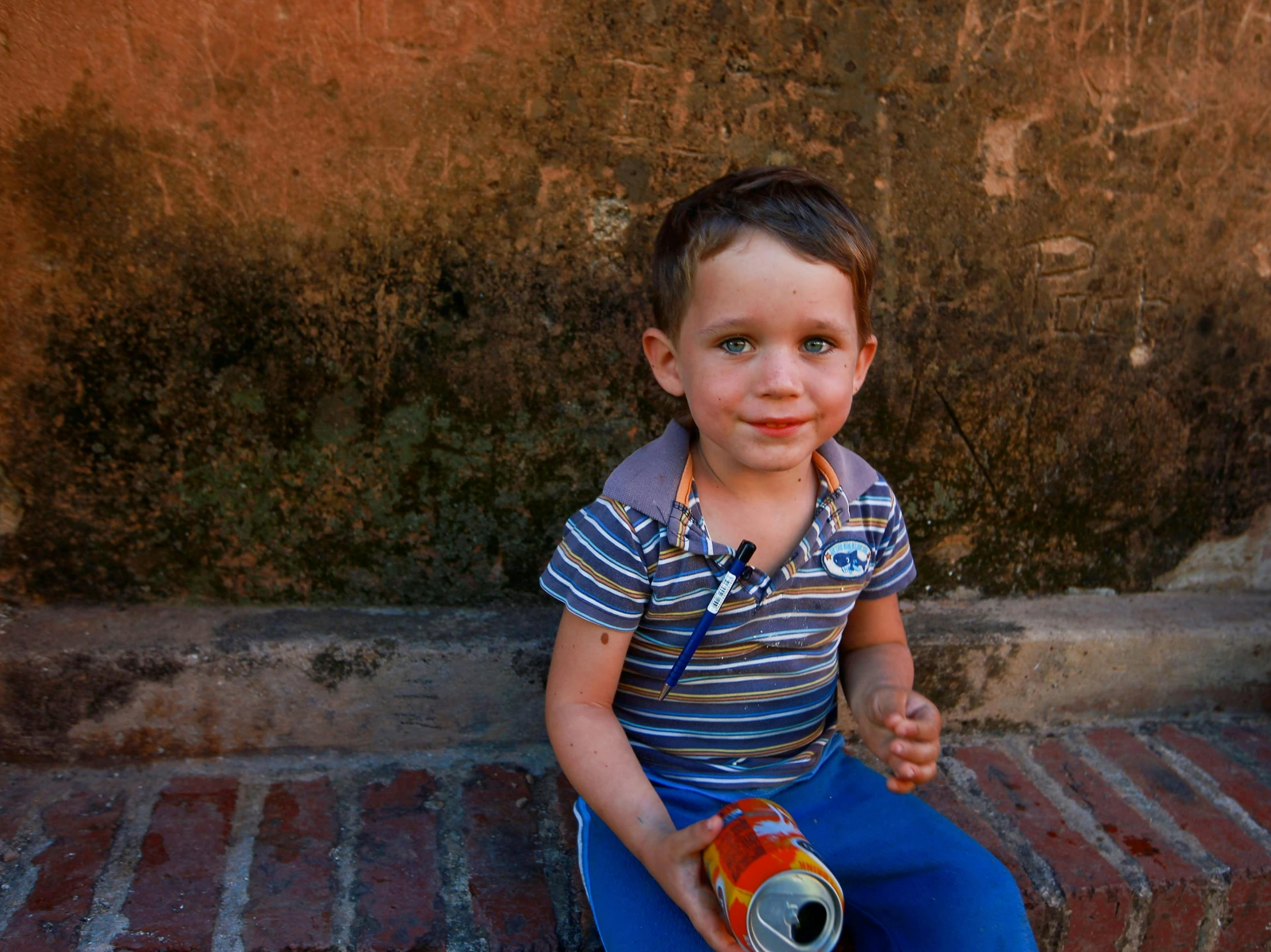 a small child sitting on a red brick floor holding a can of soda