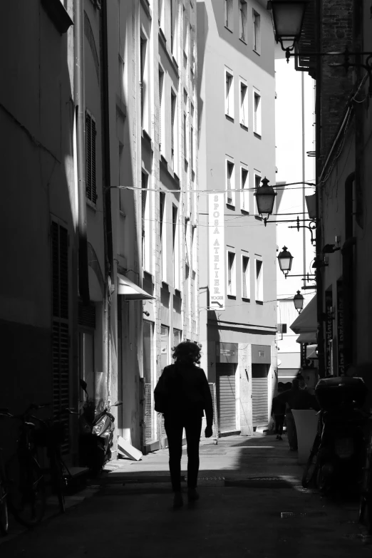 black and white image of man with open umbrella walking down a narrow alleyway