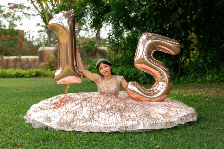 a woman in a ball gown is sitting with her large number 50 balloon