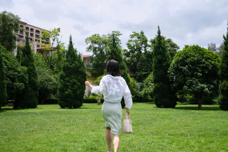 a woman walks through a grass covered field holding a white purse