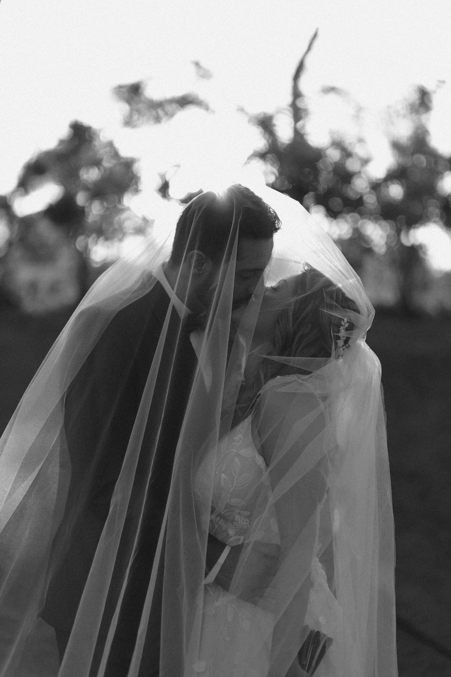 a black and white po of a bride and groom kissing in a park