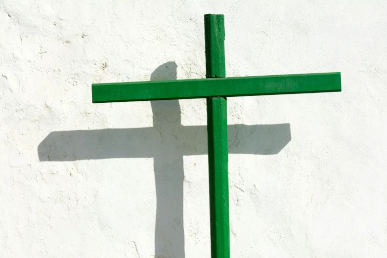 a green cross sitting against a white wall