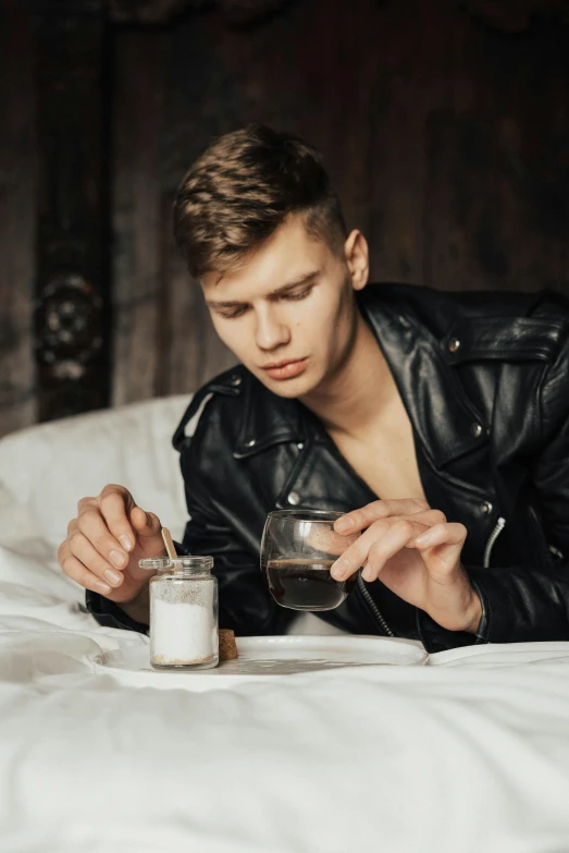 man in leather jacket laying on bed holding a cup