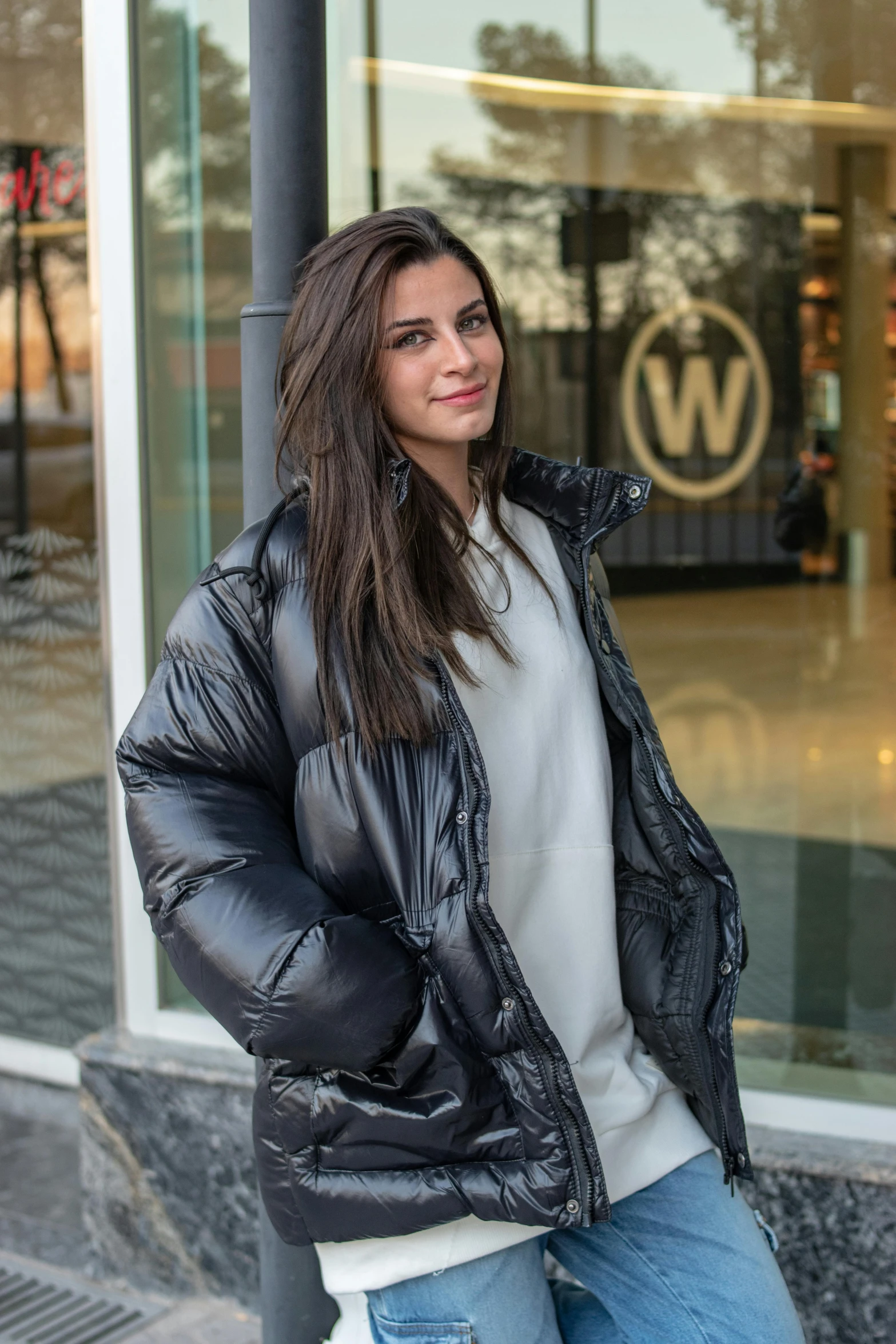 a woman in jeans and jacket leaning up against a pole