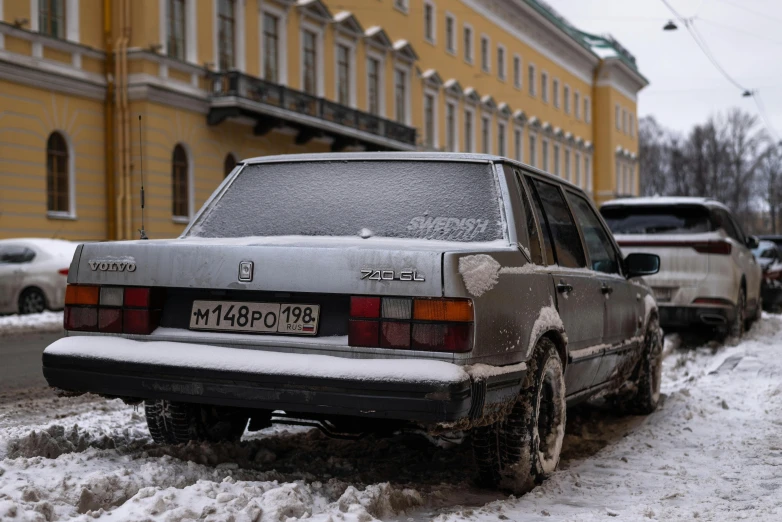 cars are parked along a snow covered road near a yellow building