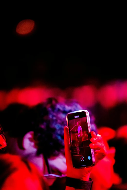 person holding up phone taking picture with crowd in background