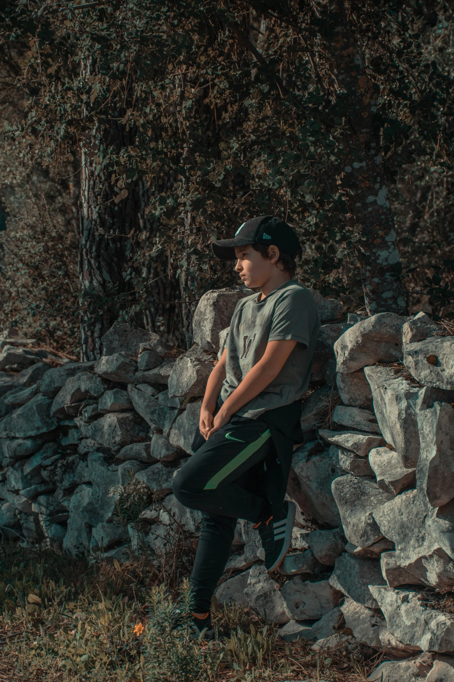 the man sits on a rock wall with his hands in his pockets