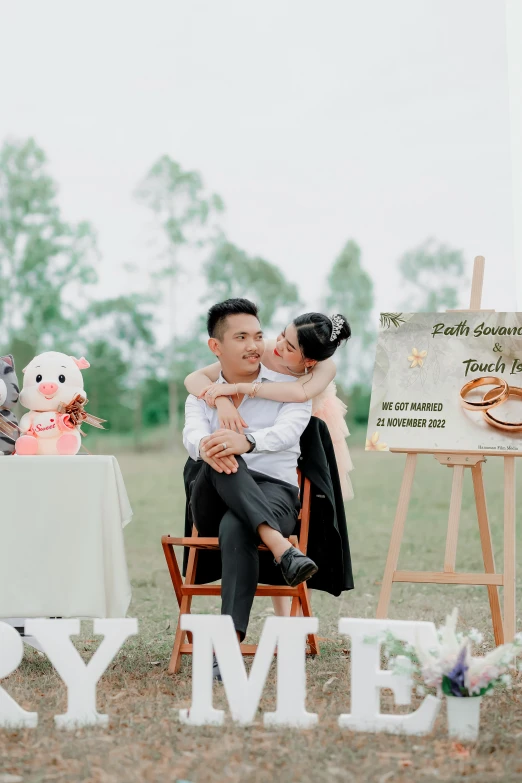 an asian man and a woman sitting in a chair in front of a sign reading happy new year