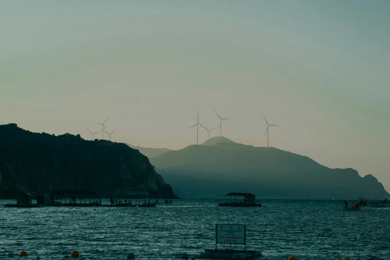 wind mills rise out of a mountain in the ocean